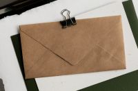 Kaboompics - Brown Kraft Paper Envelope with Black Binder Clip on White and Green Paper, Minimal Stationery Mockup