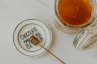 Kaboompics - Overhead Kitchen Still Life with Honey Jar, Lettered Saucer and Dipper on Pale Surface