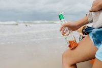 Kaboompics - Close-Up of a Woman Holding a Glass Bottle Beside the Sea and an Orange Kayak