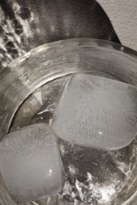 Kaboompics - High-Angle Close-Up of Ice Cubes in a Clear Glass of Water, Sunlit Rim and Textured Stone Background
