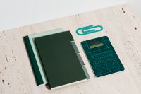 Kaboompics - Dark Green Notebooks, Teal Calculator and Paper Clip on Beige Stone for Math Study Planning