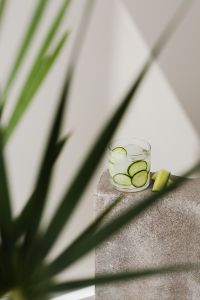 Kaboompics - Cucumber Detox Water with Ice on a Concrete Block, Soft Green Foreground Leaves and Sunlit Copy Space