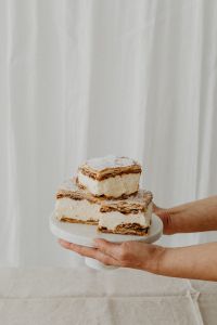 Kaboompics - Hands Presenting Napoleonka Pastries on a White Cake Stand