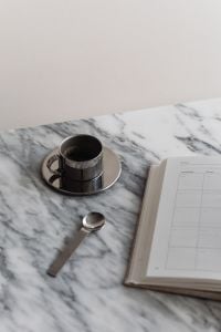 Kaboompics - Vertical Chrome Espresso Cup and Spoon beside Open Planner on Marble, Copy Space