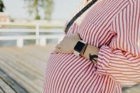 Kaboompics - Pregnant Woman with Smartwatch Standing on Sunlit Deck
