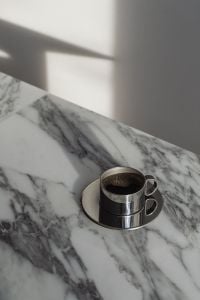 Kaboompics - Single Chrome Espresso Cup on Arabescato Marble with Long Window Shadow, Minimal Coffee Background