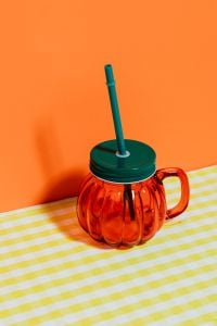 Kaboompics - Halloween Pumpkin Mug with Green Straw on Yellow Checkered Fabric