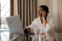 Kaboompics - Black Woman Talking on Phone While Working on Laptop at Home Office Desk
