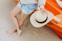 Kaboompics - Close View of Woman Holding a Straw Hat Beside an Orange Kayak on the Sandy Beach