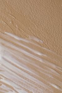 Kaboompics - Thin White Skincare Cream Swatch Along Textured Beige Surface, Minimal Macro Detail