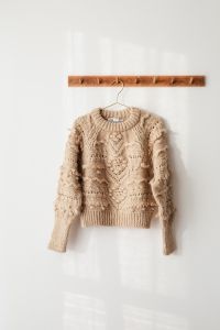 Kaboompics - Cream Cable-Knit Sweater Hanging on Wood Rail