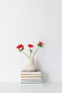 Kaboompics - Three Red Poppies in a White Vase above Stacked Books