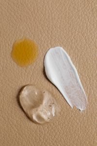 Kaboompics - White Skincare Cream and Amber Gel Swatch on Textured Tan Surface, Product Macro