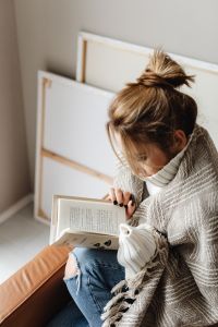 Kaboompics - Woman Reading a Book in a Gray Knit Blanket at Home