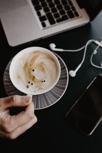Kaboompics - Hand Holding Cappuccino beside Laptop, Earbuds and Smartphone in Home Office
