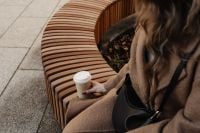 Kaboompics - Woman Holding Coffee While Sitting on a Curved Wooden Bench