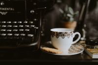 Kaboompics - Ornate Empty Coffee Cup and Saucer beside Vintage Typewriter and White Flowers, Coffee Break Styling