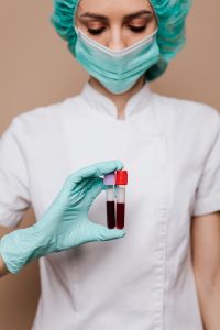 Kaboompics - Masked Healthcare Worker Holding Two Blood Sample Tubes, Vertical Patient Education Portrait