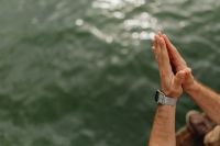Kaboompics - Raised Hands Together with Retro Digital Watch beside Green Lake Water, Vertical Detail