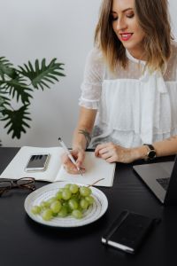 Kaboompics - Female Freelancer Writing in Notebook Beside Laptop and Grapes