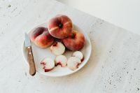 Kaboompics - Peaches and Slices on White Plate with Wooden Knife, Top View