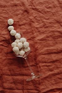 Kaboompics - Top-Down Glass of Coconut Truffles with a Diagonal Candy Trail, Minimal Rust-Linen Background