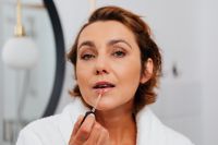 Kaboompics - Side-Profile of a Woman Applying Lip Gloss with a Wand in Front of a Bathroom Mirror