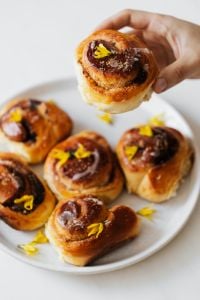 Kaboompics - Hand Holding Iced Cinnamon Roll over a Pastry Plate for Recipe Promotion