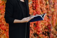Kaboompics - Side View of a Woman Holding a Blue-Covered Book against Orange Autumn Foliage