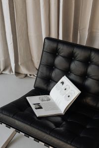 Kaboompics - Black Leather Barcelona Chair and Open Book Against Linen Curtains