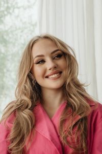 Kaboompics - Smiling Woman in a Pink Trench Coat by a Window