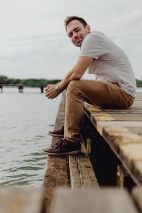 Kaboompics - Man Seated at Lake Edge in White Shirt and Tan Trousers, Vertical Waterfront Lifestyle Portrait