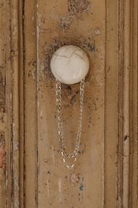 Kaboompics - Silver Chain Necklace Hanging from an Ivory Ceramic Knob on Weathered Wood