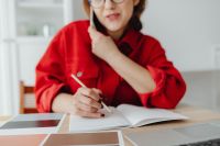 Kaboompics - Home Office Planning: Woman Writing in a Notebook during a Smartphone Call beside Laptop and Color Palette