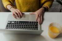 Kaboompics - Close-Up Hands Using Laptop at a White Desk with Orange Juice