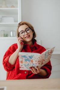Kaboompics - Smiling Woman on Phone while Browsing an Open Magazine at Desk