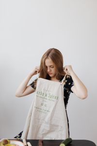 Kaboompics - Woman Putting on an Apron in a Bright Kitchen with Copy Space
