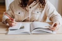 Kaboompics - Woman Writing in Notebook Over Open Book