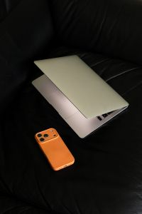 Kaboompics - Vertical Still Life of Orange Phone and Laptop on Black Sofa
