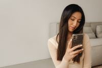 Kaboompics - Woman Looking at Her Smartphone on a Cream Sofa, Neutral Lifestyle Portrait
