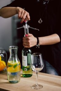 Kaboompics - Hands Opening a Wine Bottle with Corkscrew, Carafe and Wine Glasses