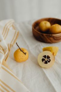 Kaboompics - Whole and Sliced Chaenomeles in Front of a Blurred Wooden Bowl, Linen Food Styling