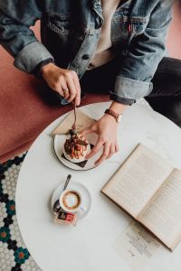 Kaboompics - A woman eats meringue, drinks coffee and reads a book in a patisserie