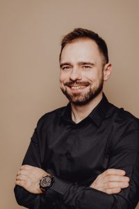 Kaboompics - Smiling Man in Black Shirt with Crossed Arms, Warm Neutral Headshot for Professional Profiles