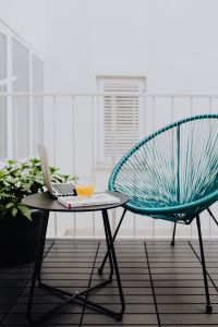 Kaboompics - A stylish garden chair and a small table on the balcony. Macbook laptop, book and a glass of orange juice.