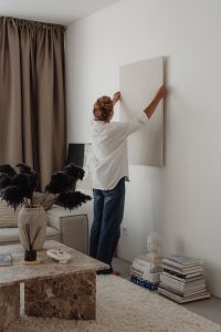 Kaboompics - Woman Hanging Neutral Wall Art in a Bright Living Room