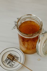Kaboompics - Open Glass Honey Jar with Wooden Dipper on Plate, Vertical Kitchen Still Life with Copy Space