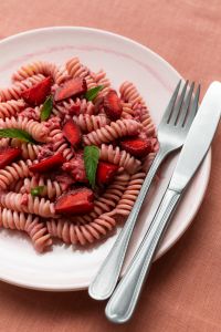 Kaboompics - Pink Strawberry Fusilli on White Plate With Fork and Knife