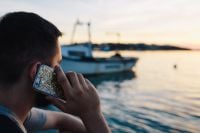 Kaboompics - Man on a Smartphone Call with a Sailboat Moored Behind Him
