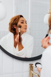 Kaboompics - Middle-Aged Woman Applying Blush with a Makeup Brush in a Bathroom Mirror